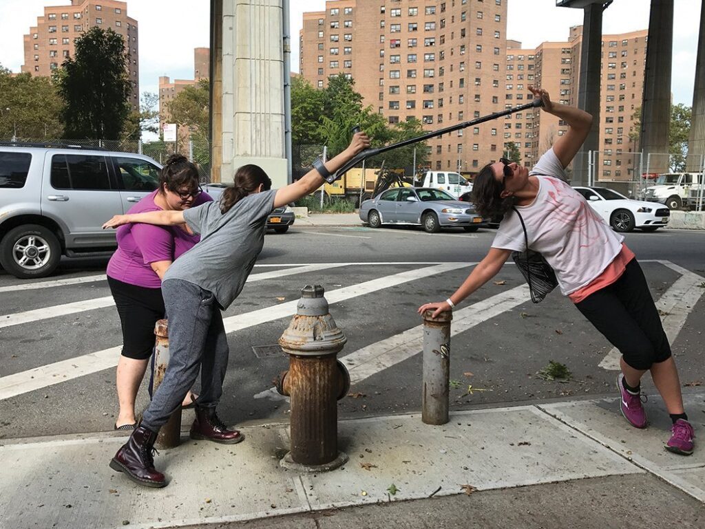 NYC street with three movers around a fire hydrant leaning into connection through a cane