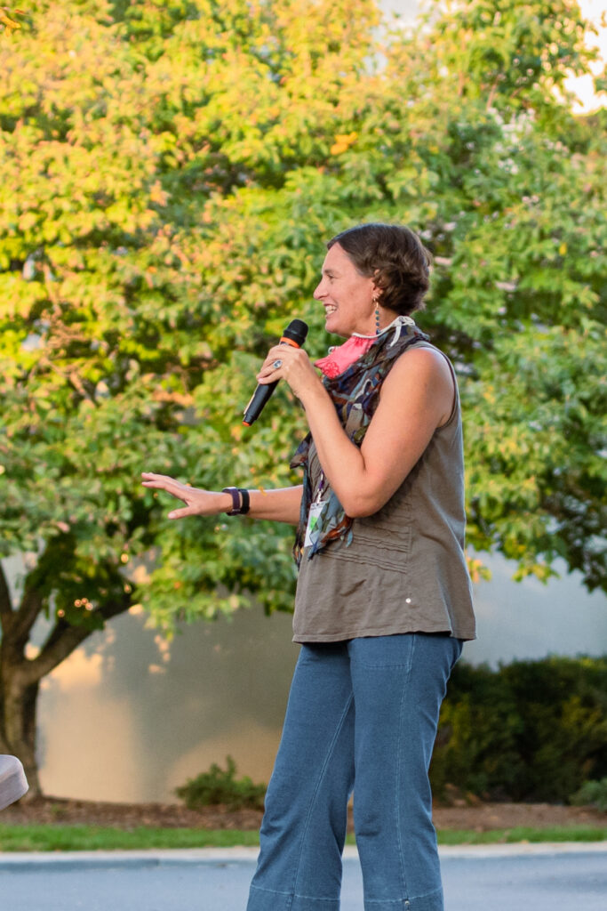 Stephanie leading a group workshop with microphone in hand, background of fall yellow leaves